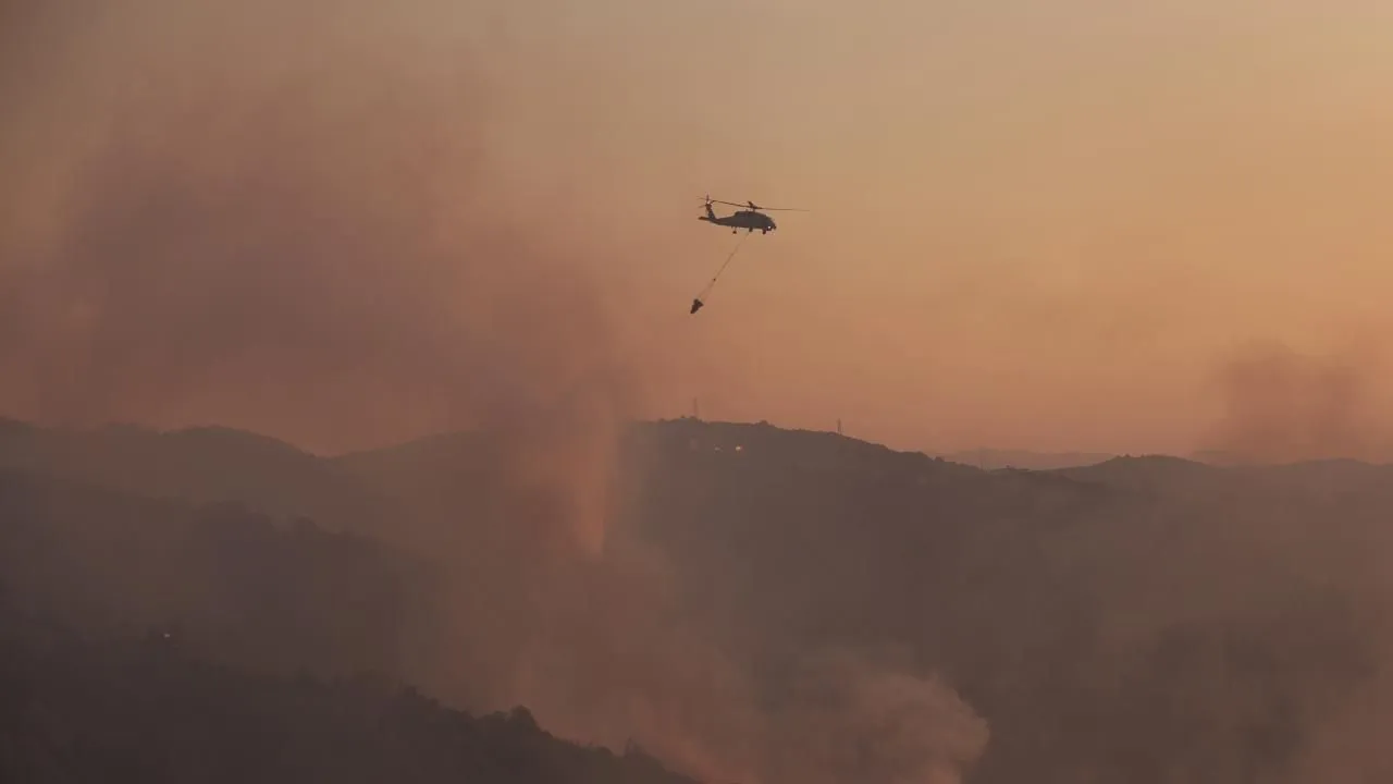 Orman yangınına müdahale eden yangın söndürme helikopteri ve yoğun dumanın yükseldiği dağlık alan